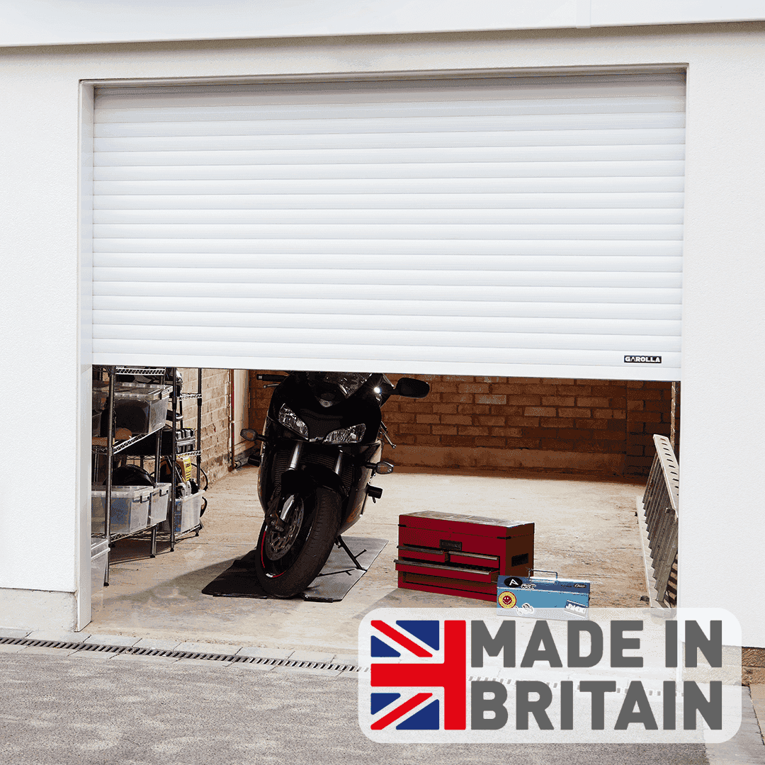 A white electric roller garage door partially open, showing a motorbike and tools stored securely inside a garage, with a Made in Britain logo