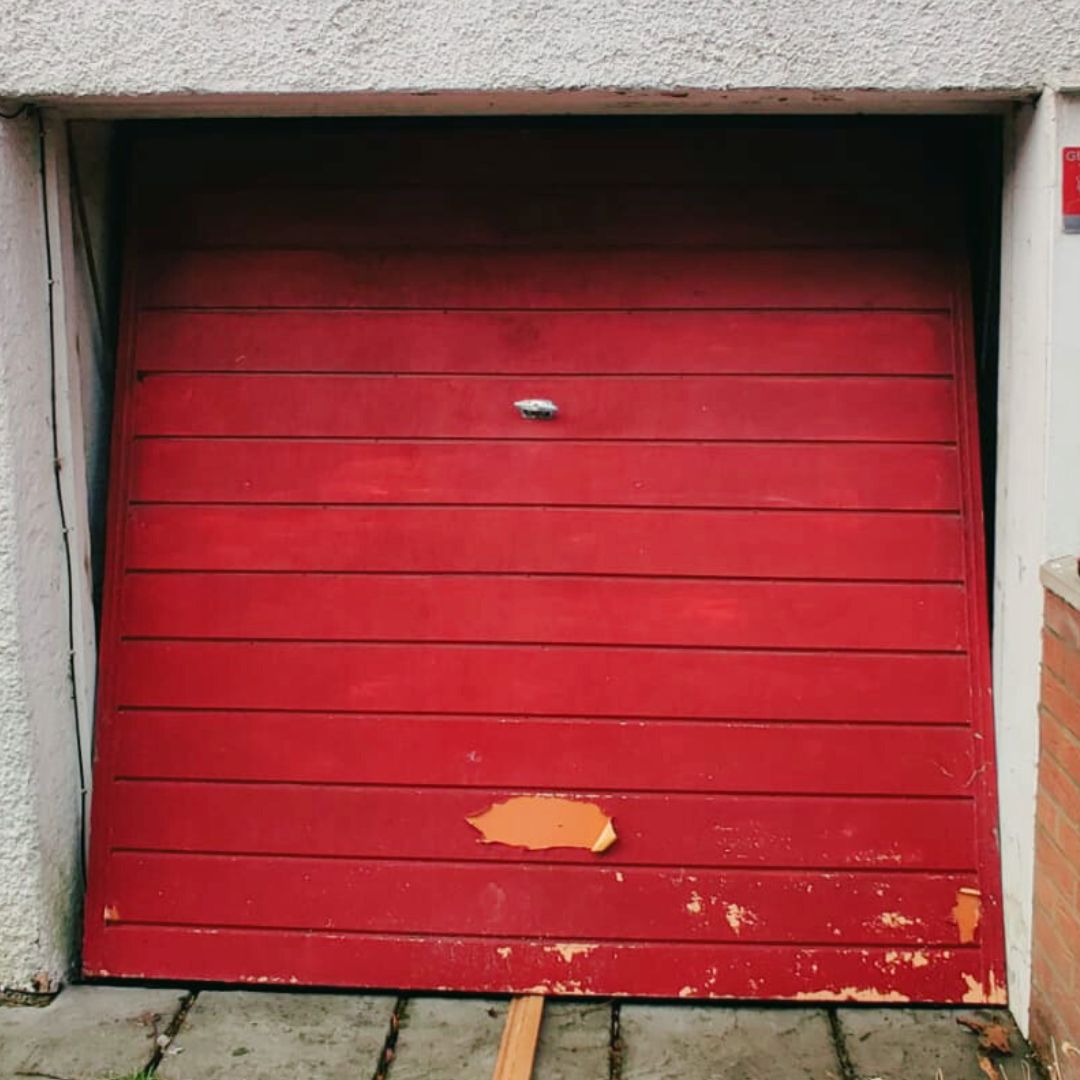 A broken manual up-and-over red garage door