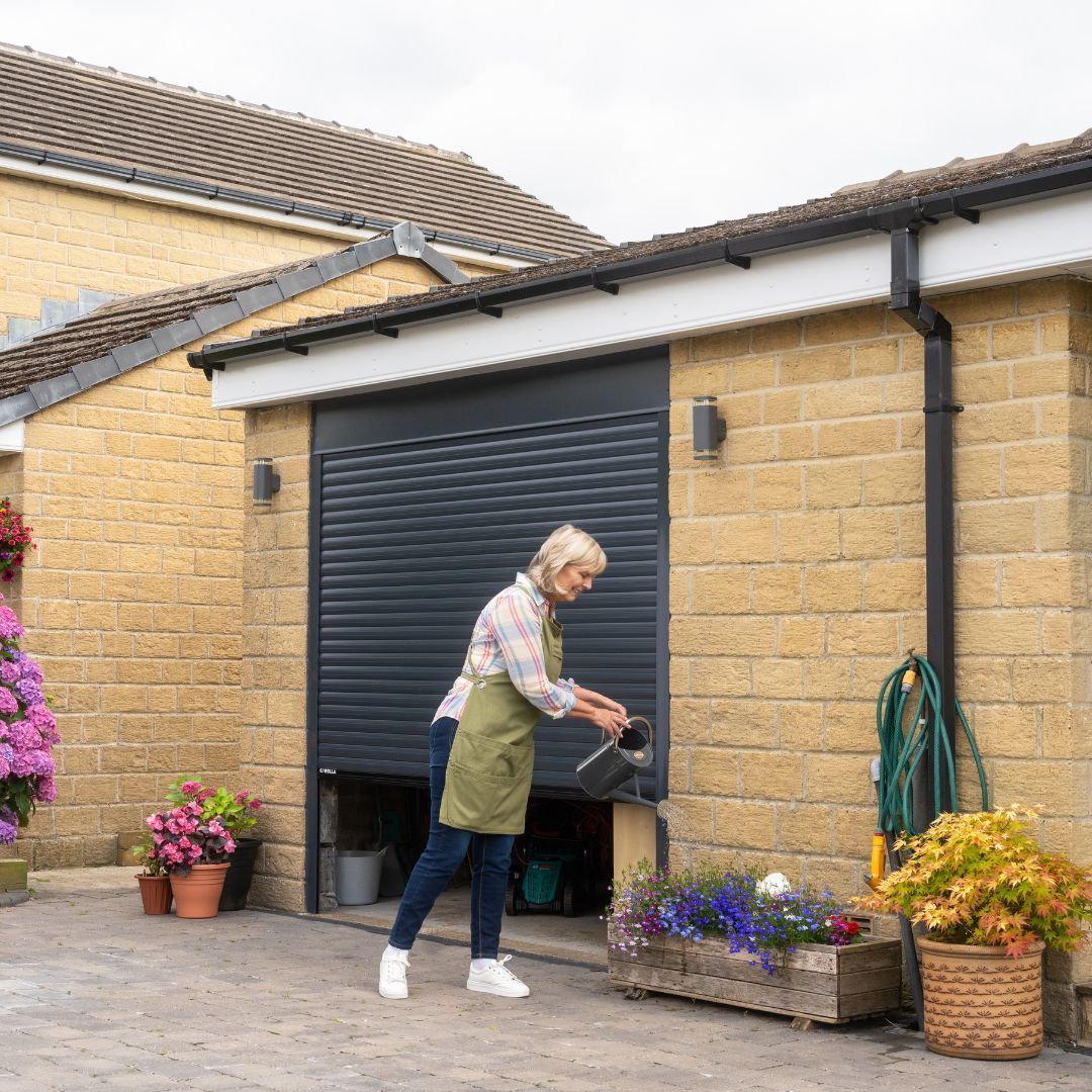 Pensioner watering plants in front of Garolla garage door